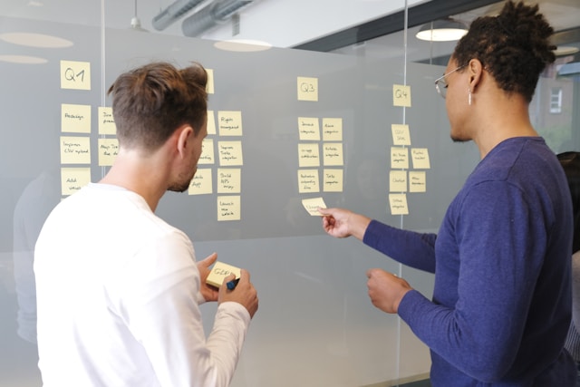 Two coworkers putting sticky notes on a board to figure out task prioritization