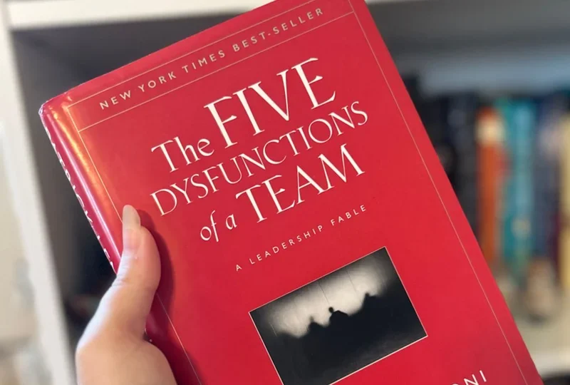 A person holding The Five Dysfunctions of a Team by Patrick Lencioni book