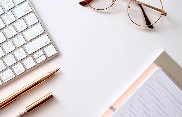 A white desk with a notebook laptop and glasses on it