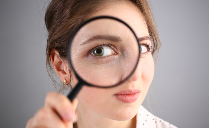 A woman holding a magnifying glass to her face and enlarging her eye