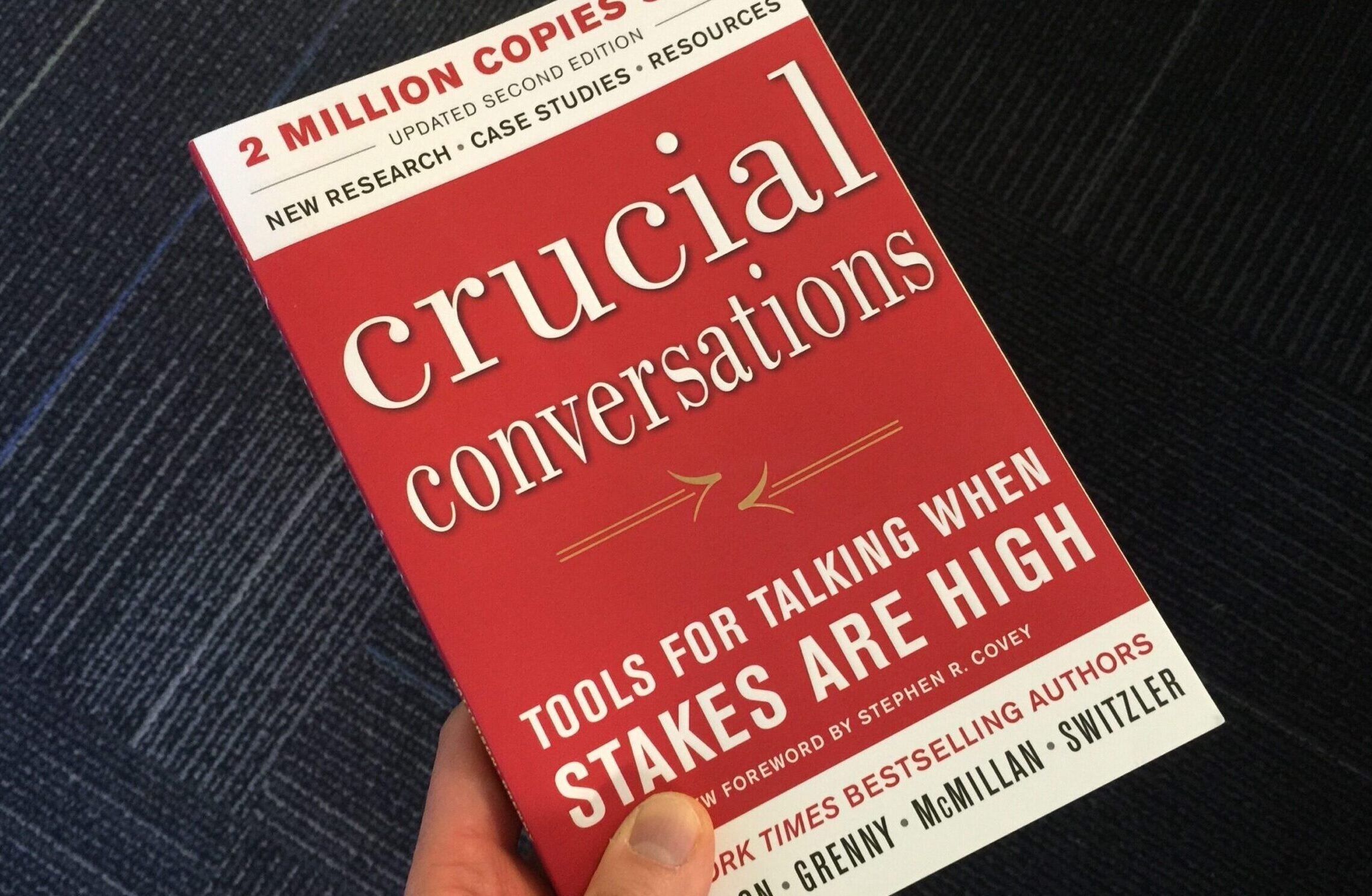 Someone holding the book Crucial Conversations: Tools for Talking When Stakes Are High