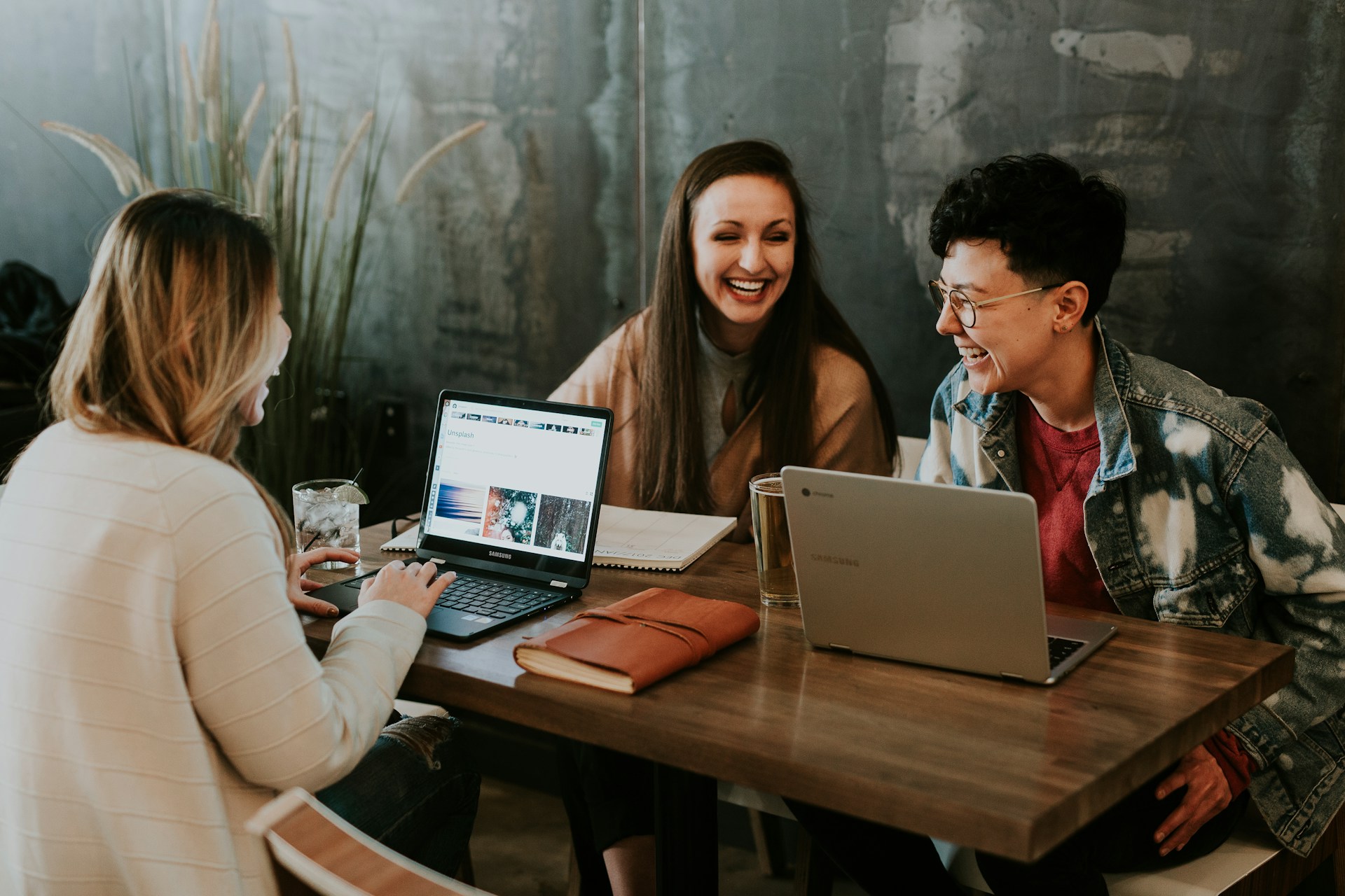 Three business people sitting at a coffee shop working on laptops and networking