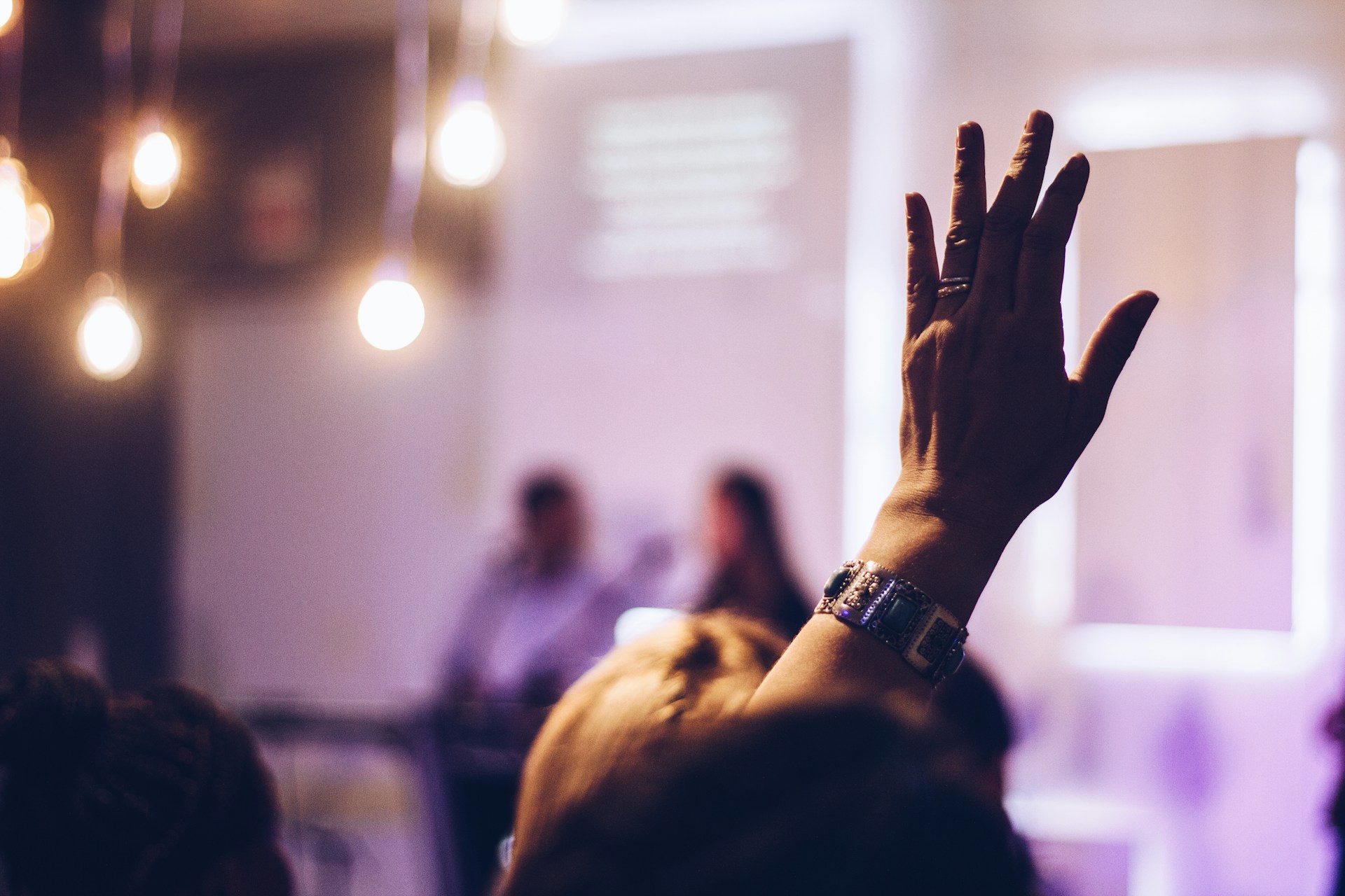 Closeup of a person raising their hand to ask a question at an event