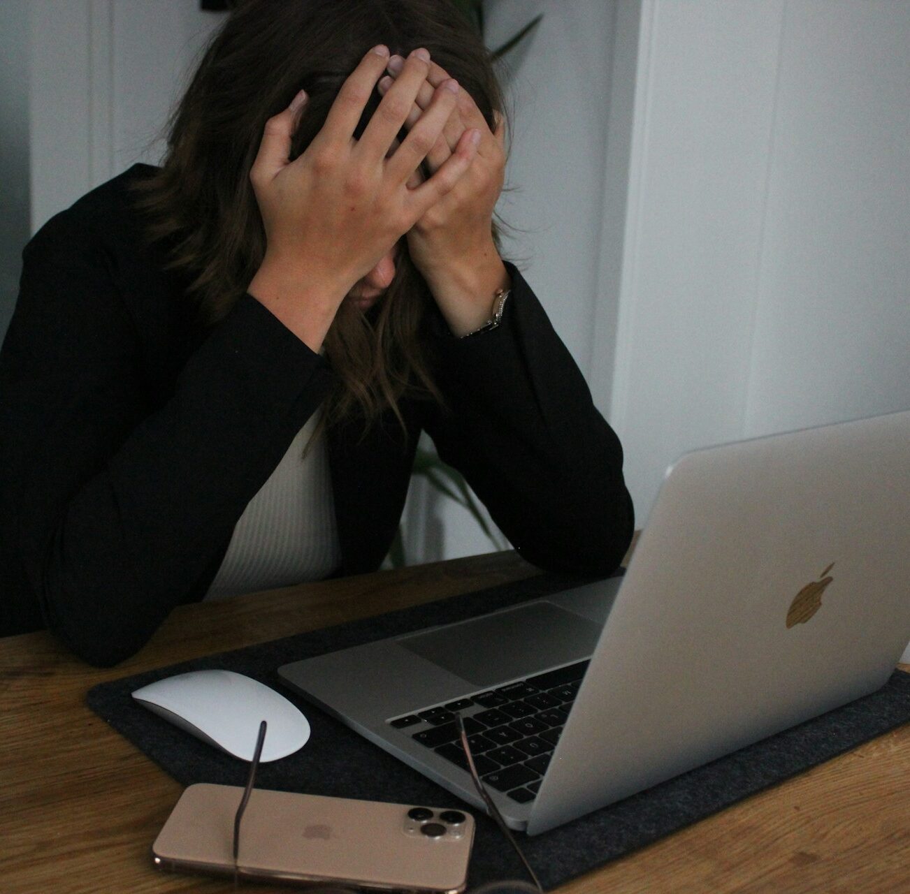 A business owner with their head in their hands in frustration while sitting at their desk on their laptop